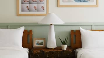 Une chambre d’hôtel avec deux lits, une table de chevet avec une lampe, une petite plante en pot et deux tableaux encadrés au mur.