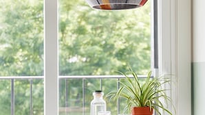 A balcony with a round wooden table, a potted plant, a glass bottle, and a chair.