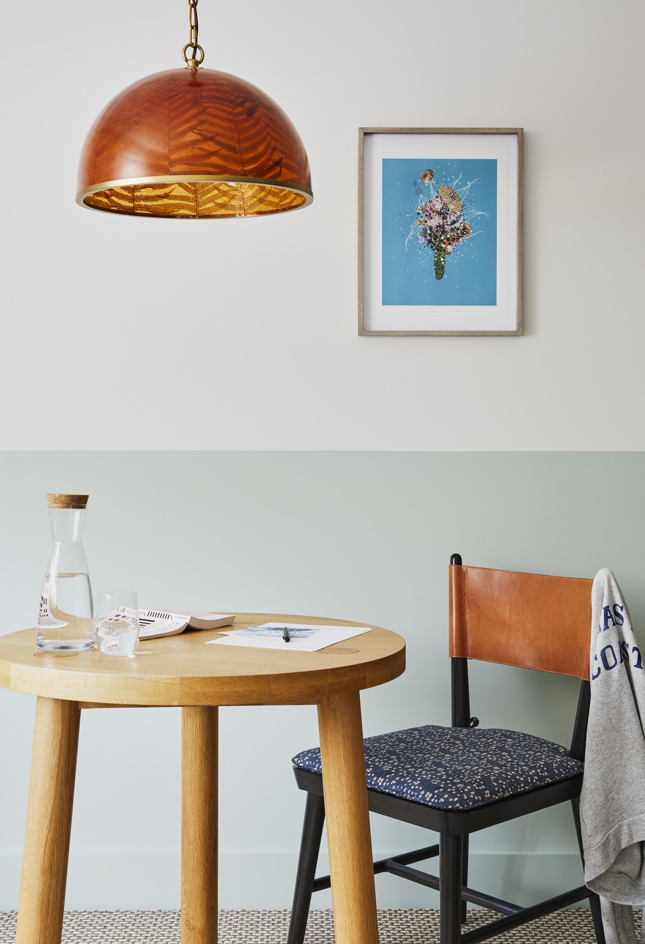 Ein runder Holztisch mit einer klaren Glasflasche und einem gerahmten Kunstwerk darüber.