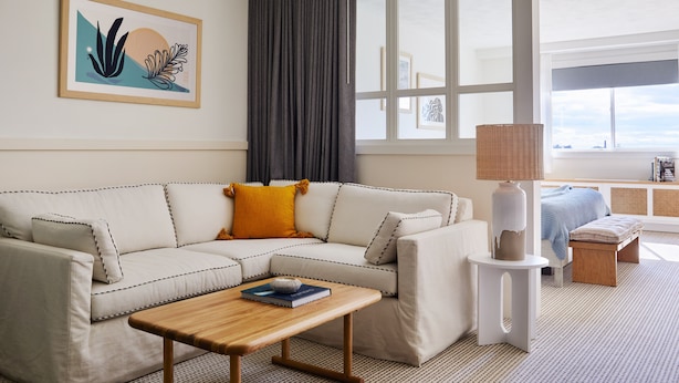 A modern living room with a sectional sofa, a wooden coffee table, a side table with a lamp, and a large window with a view.