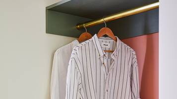 Une pièce bien rangée, avec un portant où sont suspendus des t-shirts à rayures, une pile de livres et un chapeau tressé posé sur une table.