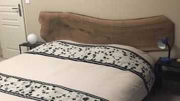 A bedroom with a wooden headboard, a bed with a floral-patterned bedspread, a nightstand with a lamp, and a painting of a beach scene on the wall.