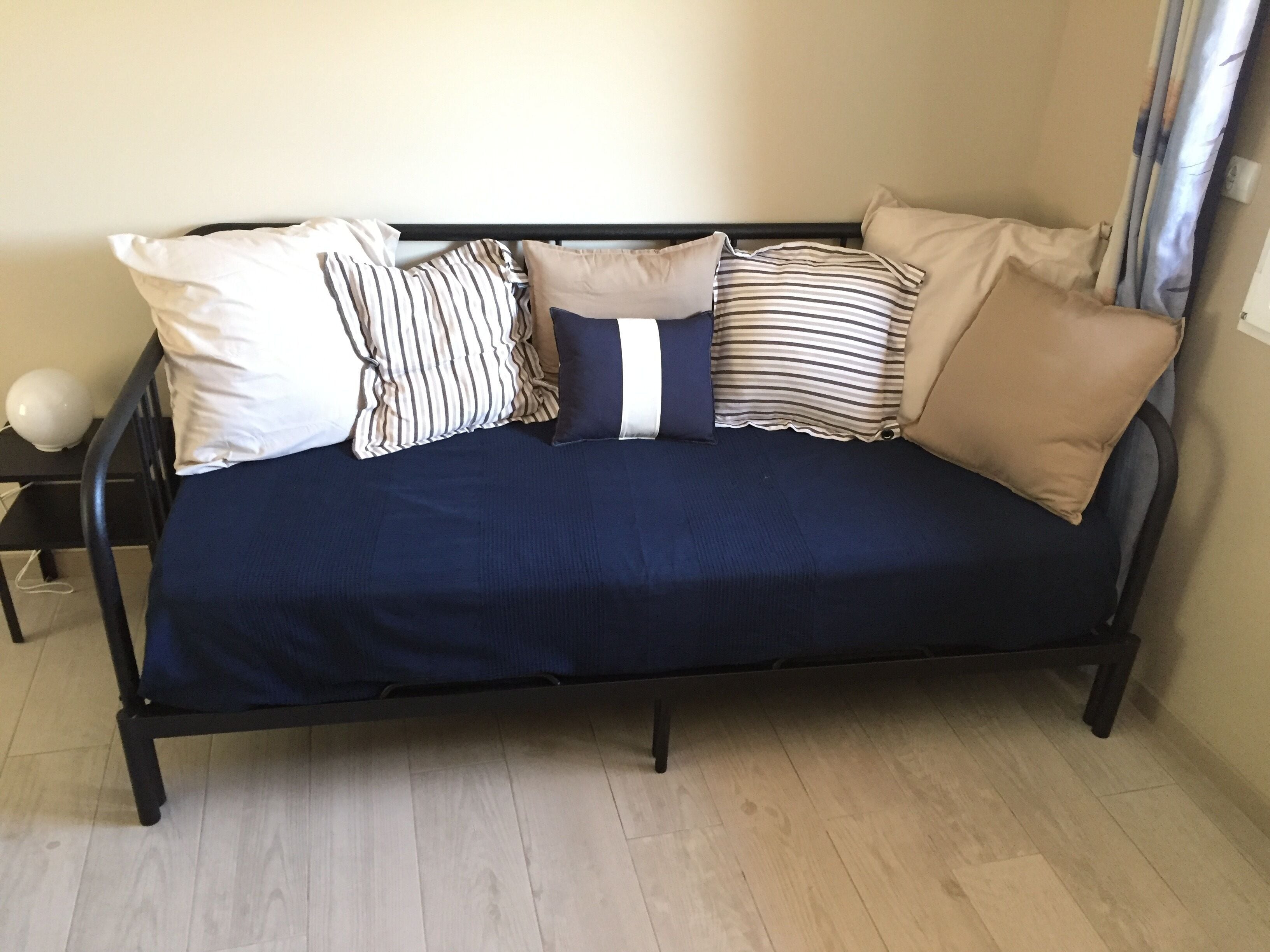 Um sofá azul escuro com várias almofadas em um quarto com piso de madeira clara.