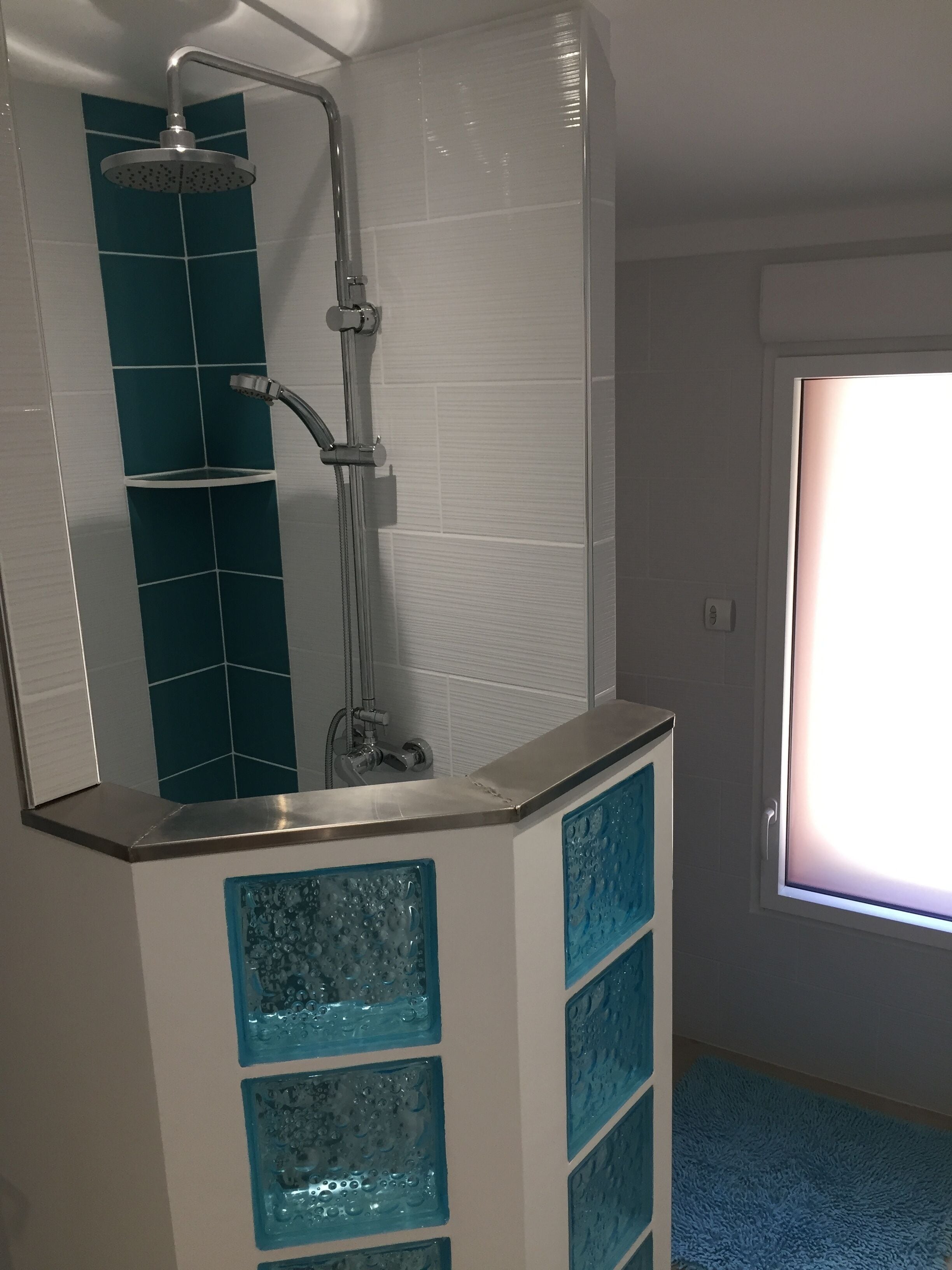 Un baño con ducha, tocador con puerta de vidrio y ventana.