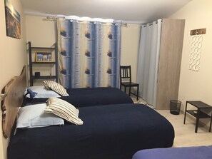 Une chambre avec deux lits, une chaise, une petite table et une étagère sur laquelle est posée une image.
