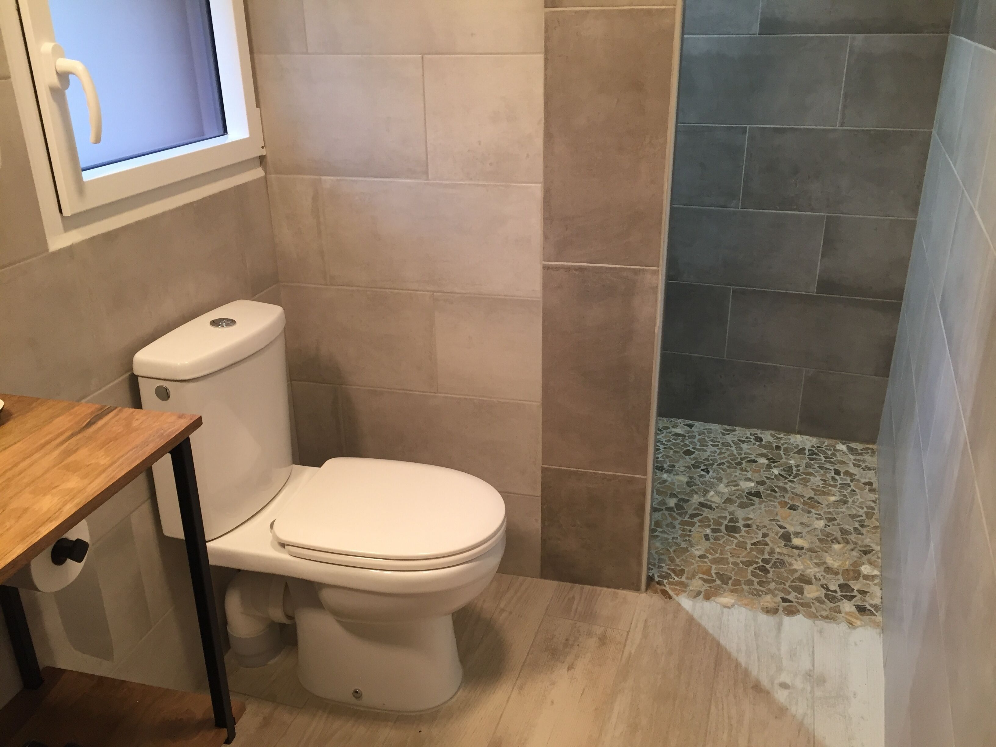 Ein Badezimmer mit Toilette, einem Fenster und einer Duschkabine mit Mosaikfliesen.