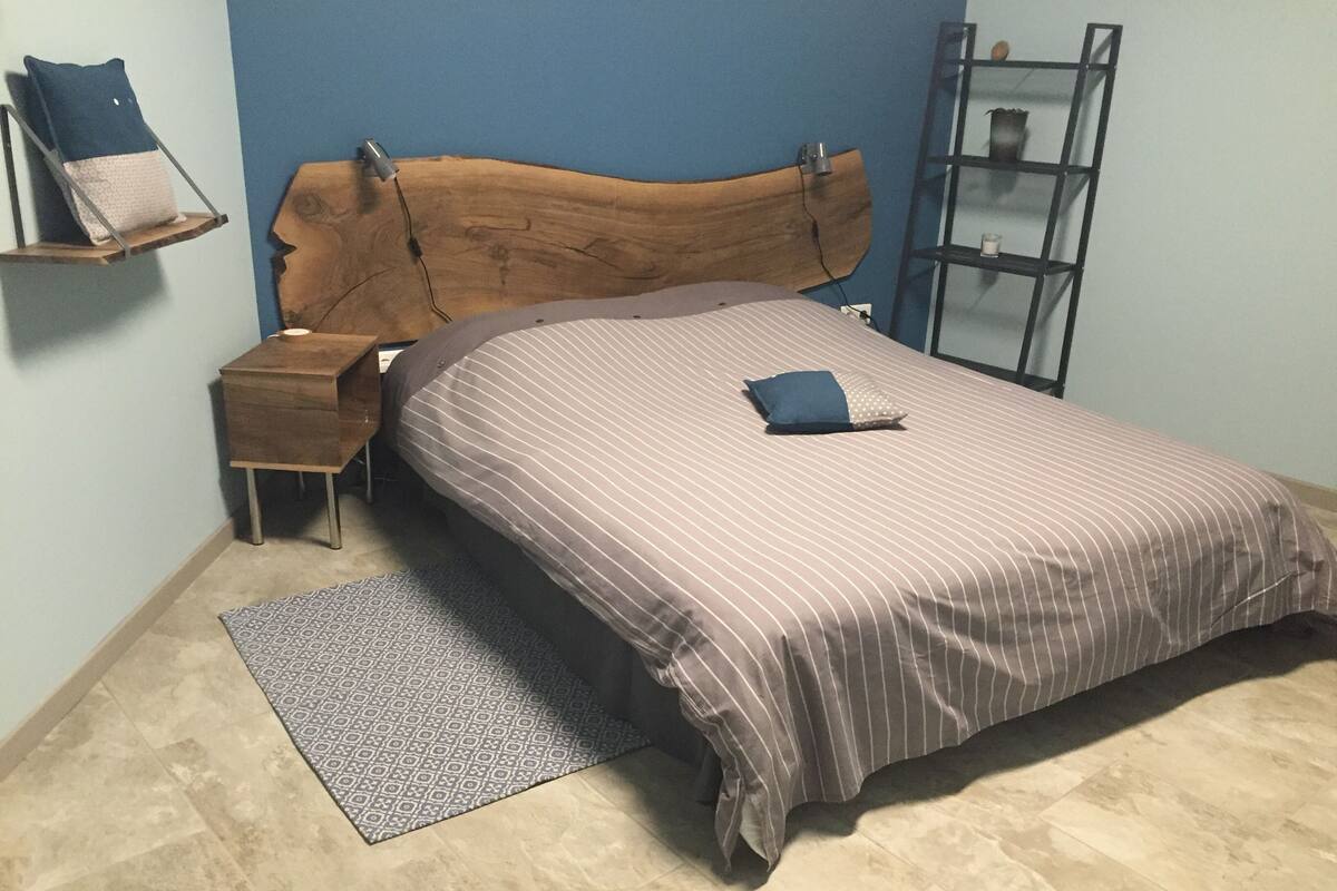 A bedroom with a wooden headboard, a bedside table, a patterned rug, and a bed with striped bedding.