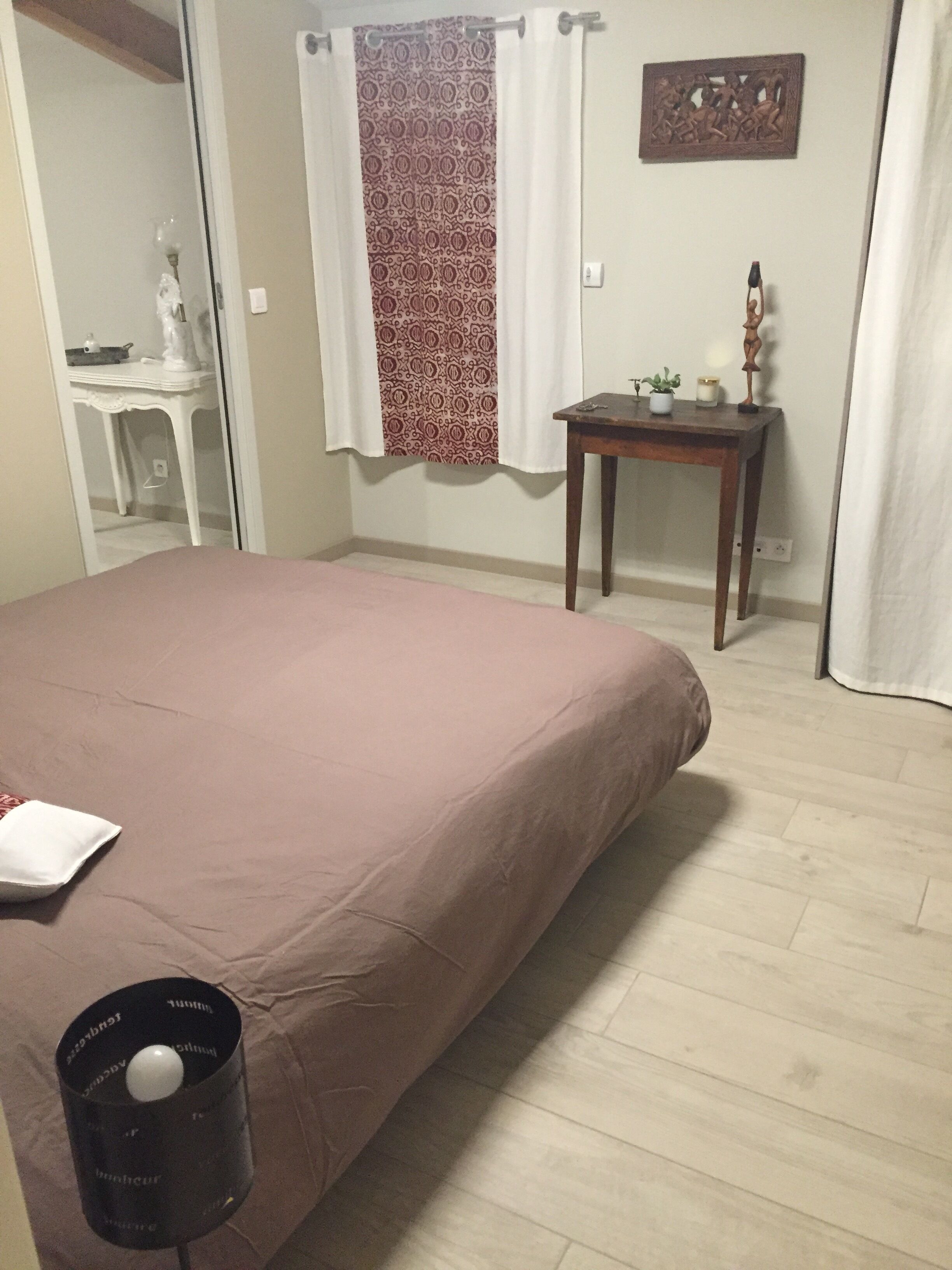 Une chambre à coucher comprenant un lit, une table de chevet, une petite table avec une plante et une œuvre d’art accrochée au mur.
