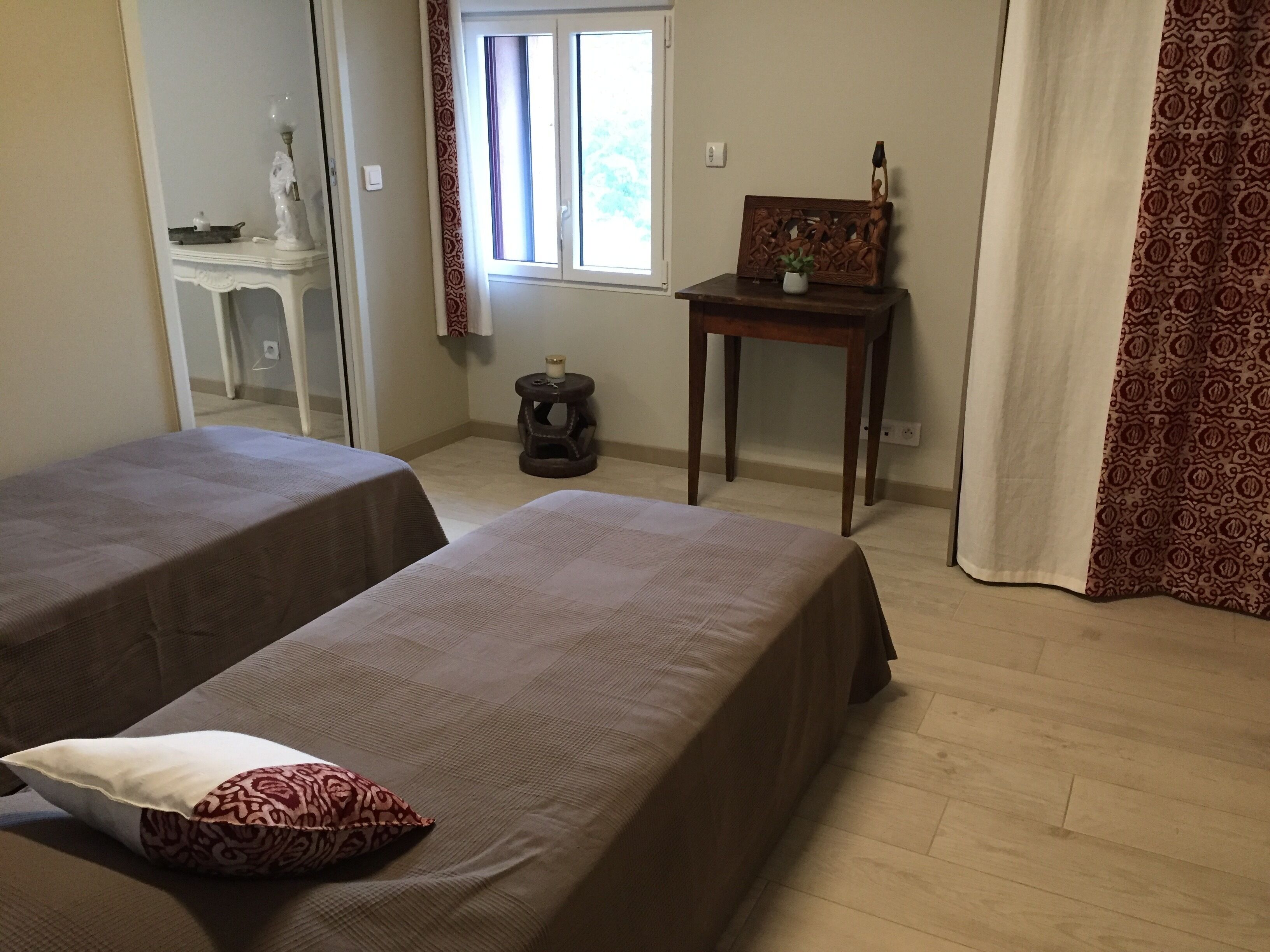 A bedroom with two beds, a small table with a plant, a statue, and a window with curtains.