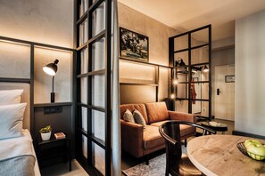 A modern hotel room with a bed, a sofa, a dining table, and a large window. - CLOUD No7 LOFTS (Stuttgart)