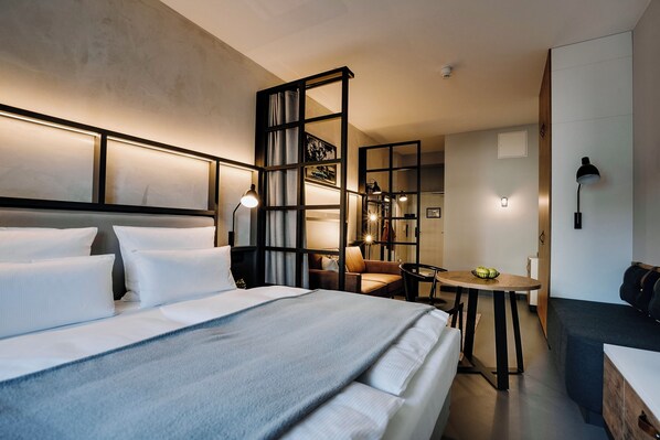A modern hotel room with a large bed, a desk, and a seating area.