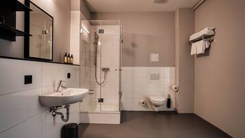 Une salle de bain moderne équipée d’un lavabo, d’un miroir, d’une douche et de toilettes.