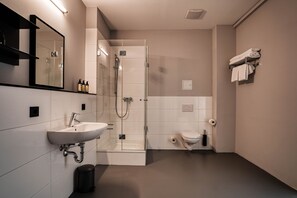 A modern bathroom with a sink, mirror, shower, and toilet.