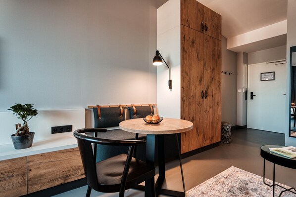 A modern dining area with a round wooden table, black chairs, a potted plant, and a wall-mounted lamp. - CLOUD No7 LOFTS (Stuttgart)