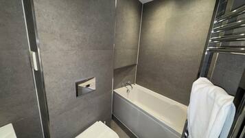 A modern bathroom with a bathtub, toilet, and a towel rack.
