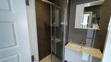 Un baño moderno con cabina de ducha de vidrio, un lavabo blanco y un espejo sobre él.