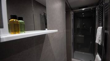 A modern bathroom with a glass shower enclosure, a white shelf with toiletries, and a towel rack.