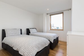 A bedroom with two beds, a window with a view of buildings, and a white cabinet.