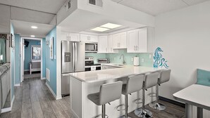 A modern kitchen with white cabinets, a central island with bar stools, stainless steel appliances, and a blue accent wall. - Updated, Direct Bay Front, Bay Front Pool, 3 Blocks to Beach and Boardwalk (Ocean City)