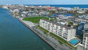 An aerial view of a coastal town with a prominent multi-story hotel featuring balconies, a swimming pool, and a marina. - Updated, Direct Bay Front, Bay Front Pool, 3 Blocks to Beach and Boardwalk (Ocean City)