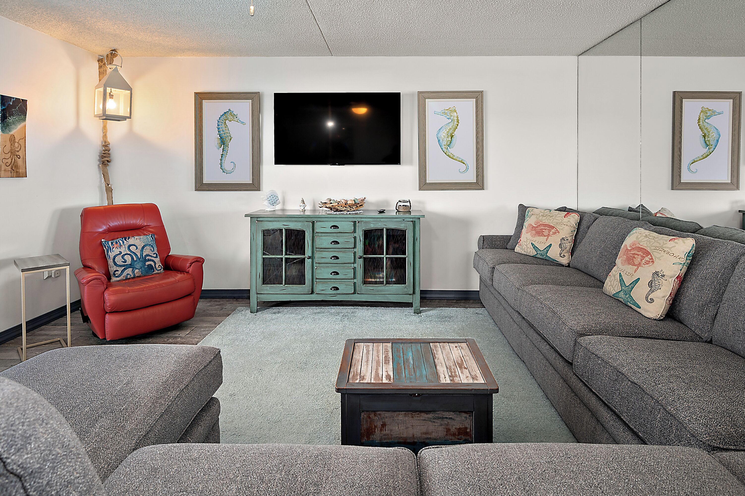 A living room with a red chair, grey sofa, and a teal cabinet.