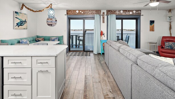 A modern living room with a grey sofa, a red chair, and a kitchen area with white cabinets and a countertop. - Updated, Direct Bay Front, Bay Front Pool, 3 Blocks to Beach and Boardwalk (Ocean City)