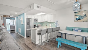 A modern kitchen with white cabinets, a central island with bar stools, a blue bench, and a teal-colored table. - Updated, Direct Bay Front, Bay Front Pool, 3 Blocks to Beach and Boardwalk (Ocean City)