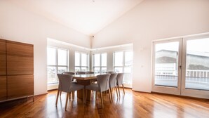 Une pièce spacieuse dotée d’un plancher en bois, d’une grande table à manger avec des chaises et de grandes fenêtres offrant une vue sur la ville.