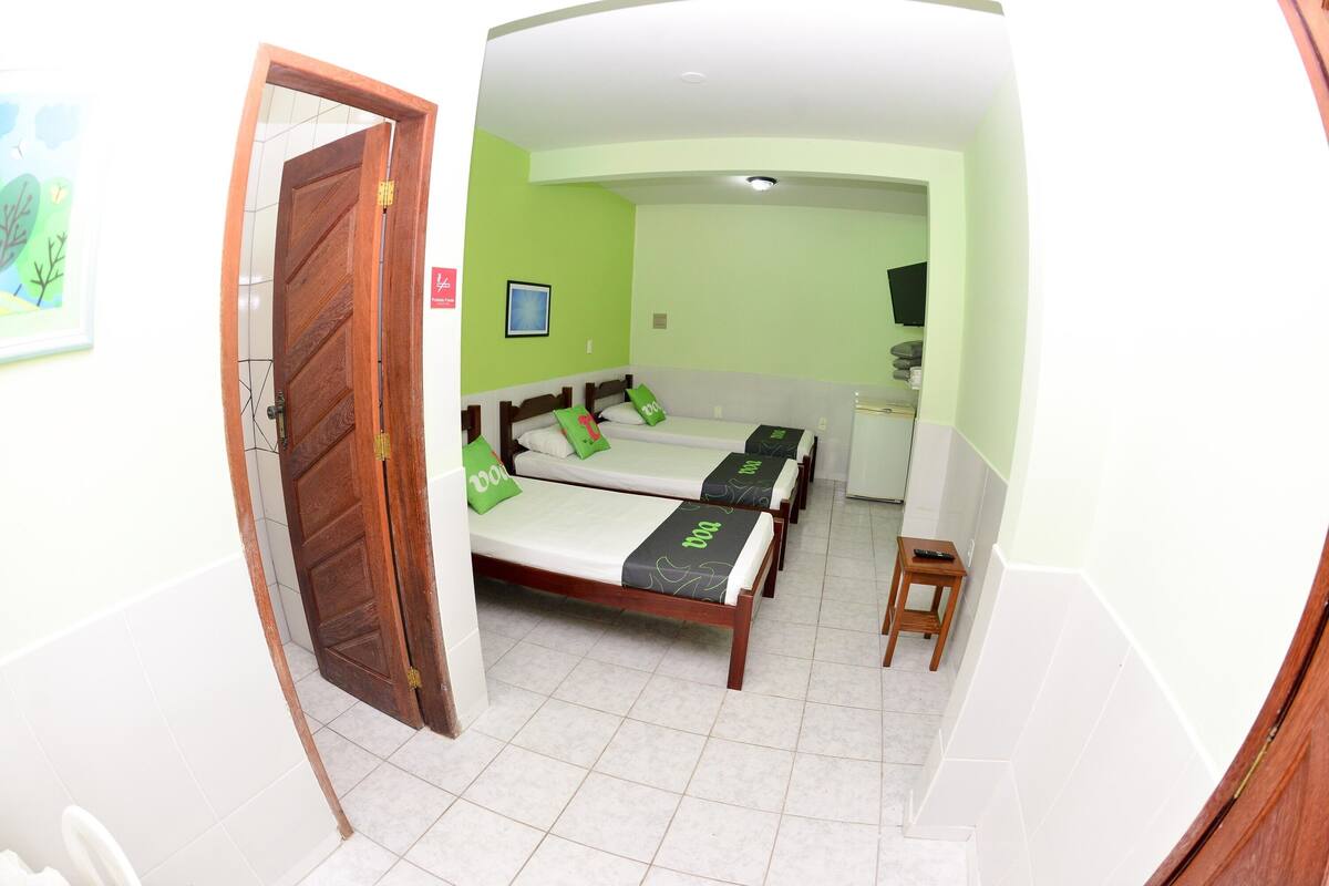 A room with a wooden door, a bed with green bedding, a small stool, and a framed picture on the wall.