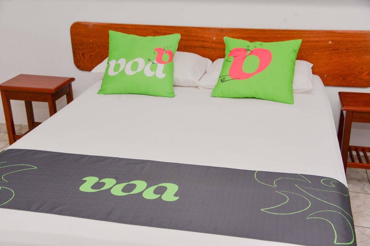 A bed with two pillows, a bedside table, and a blanket with a logo.