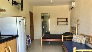 Una habitación compacta con kitchenette, una cama con colchón azul y cabecera de madera.