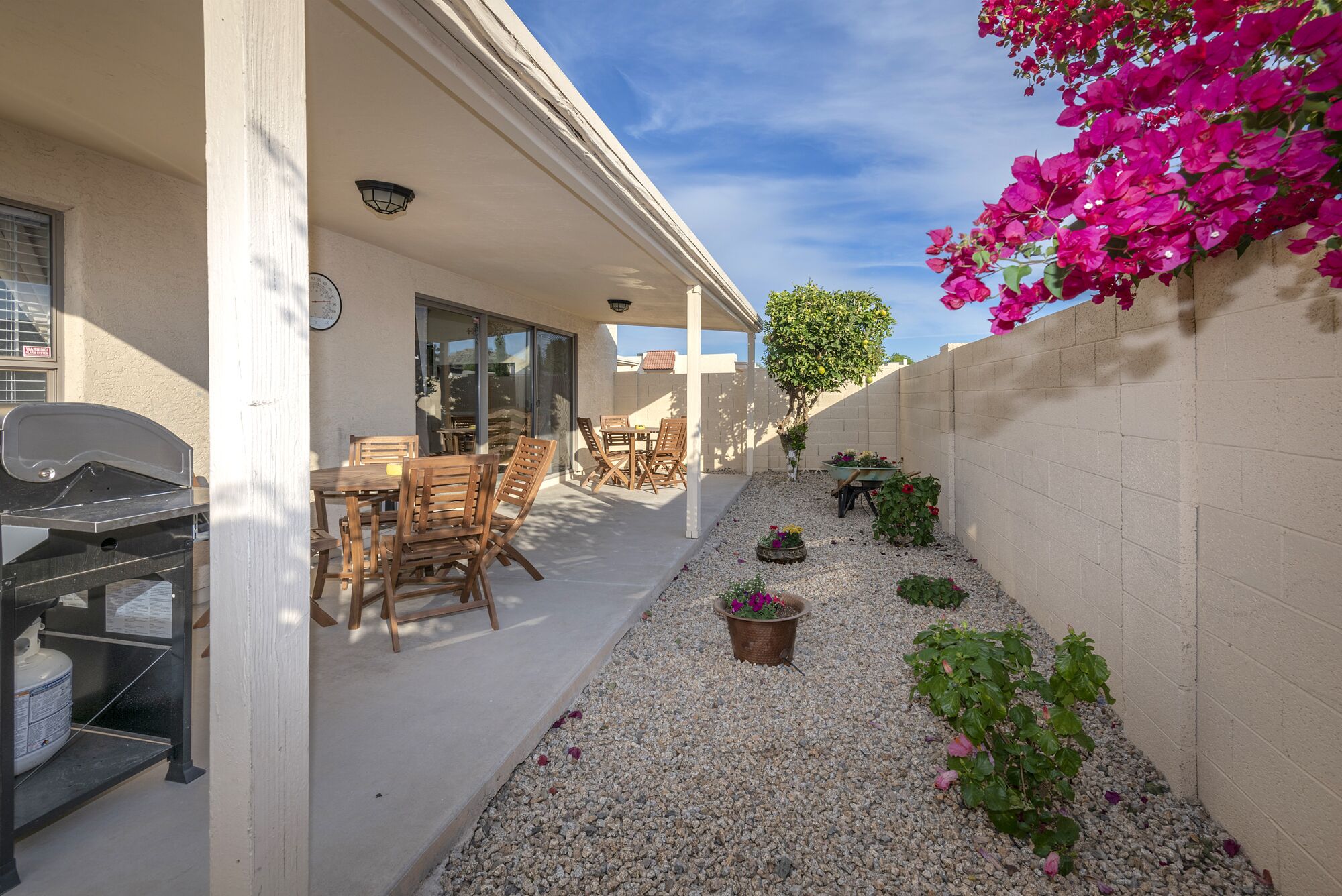 A covered patio with outdoor furniture, a barbecue grill, and a small garden area with gravel and potted plants.