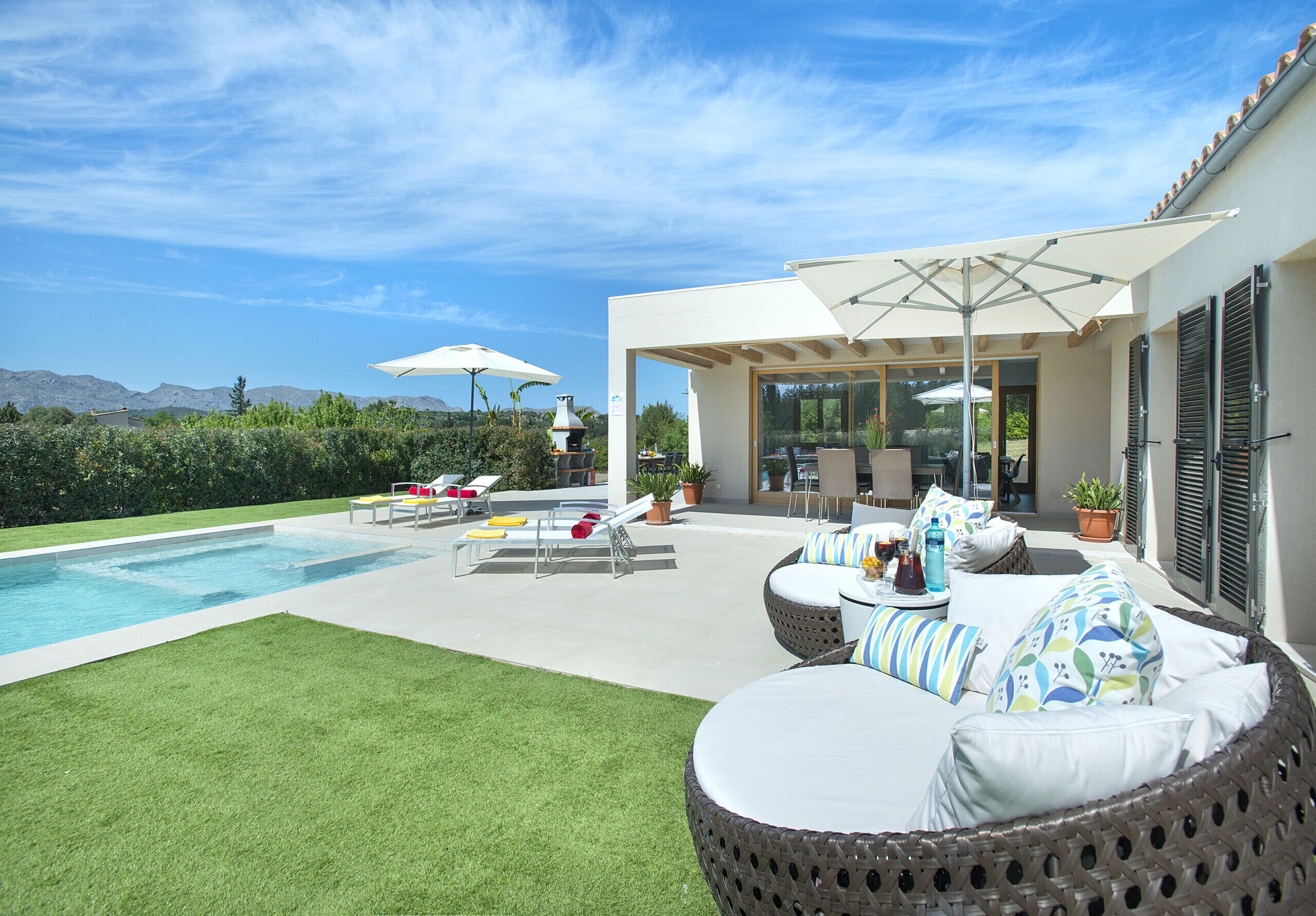 Un patio moderno al aire libre con piscina, muebles de mimbre y sombrillas.