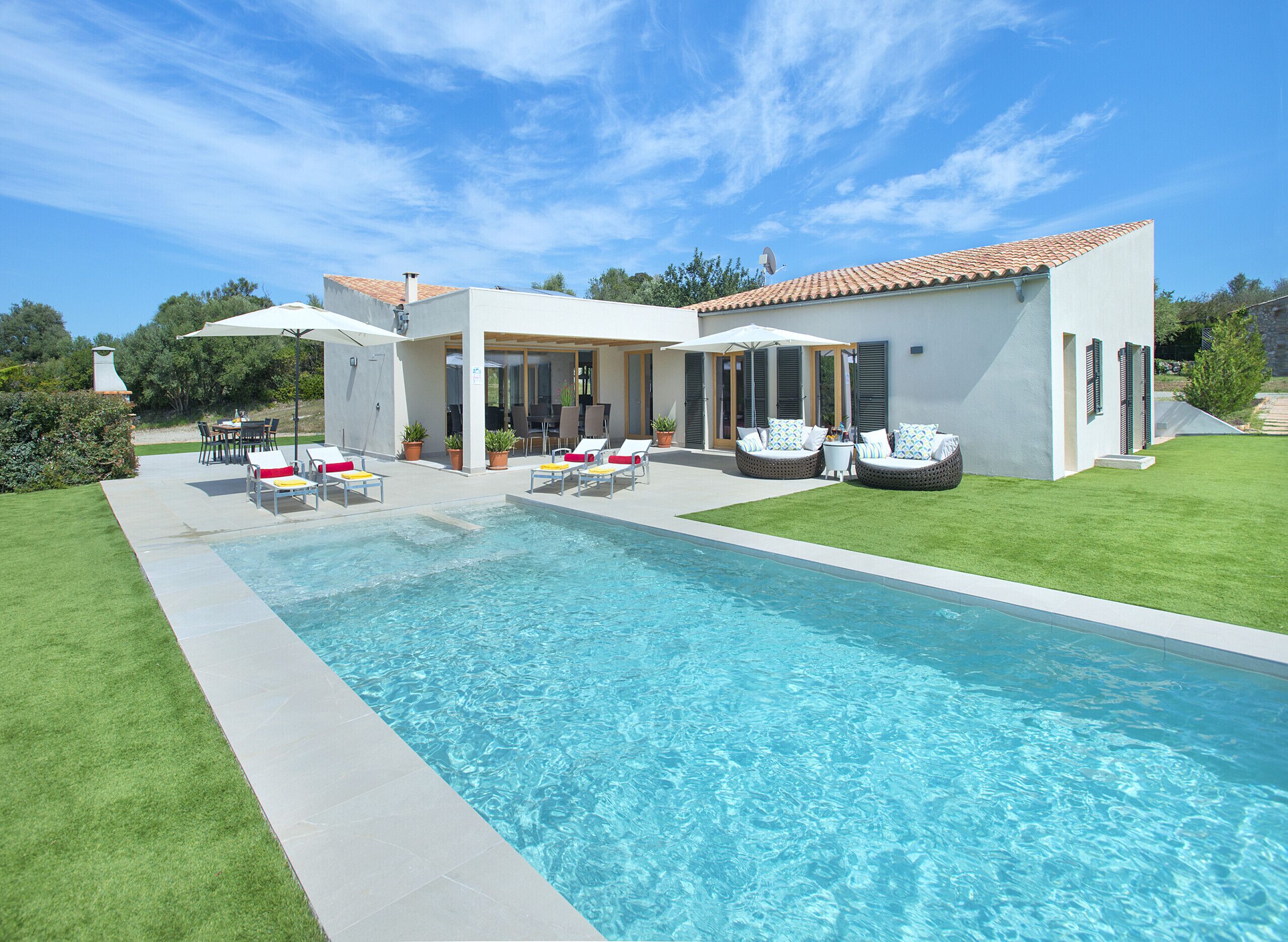 A modern house with a swimming pool, outdoor seating, and a well-maintained lawn.