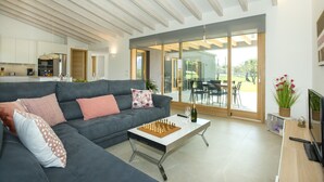 A modern living room with a grey sofa, a coffee table, and a TV. There is a glass door leading to an outdoor patio. - VILLA MIR - LUXURY RETREAT (Pollensa)