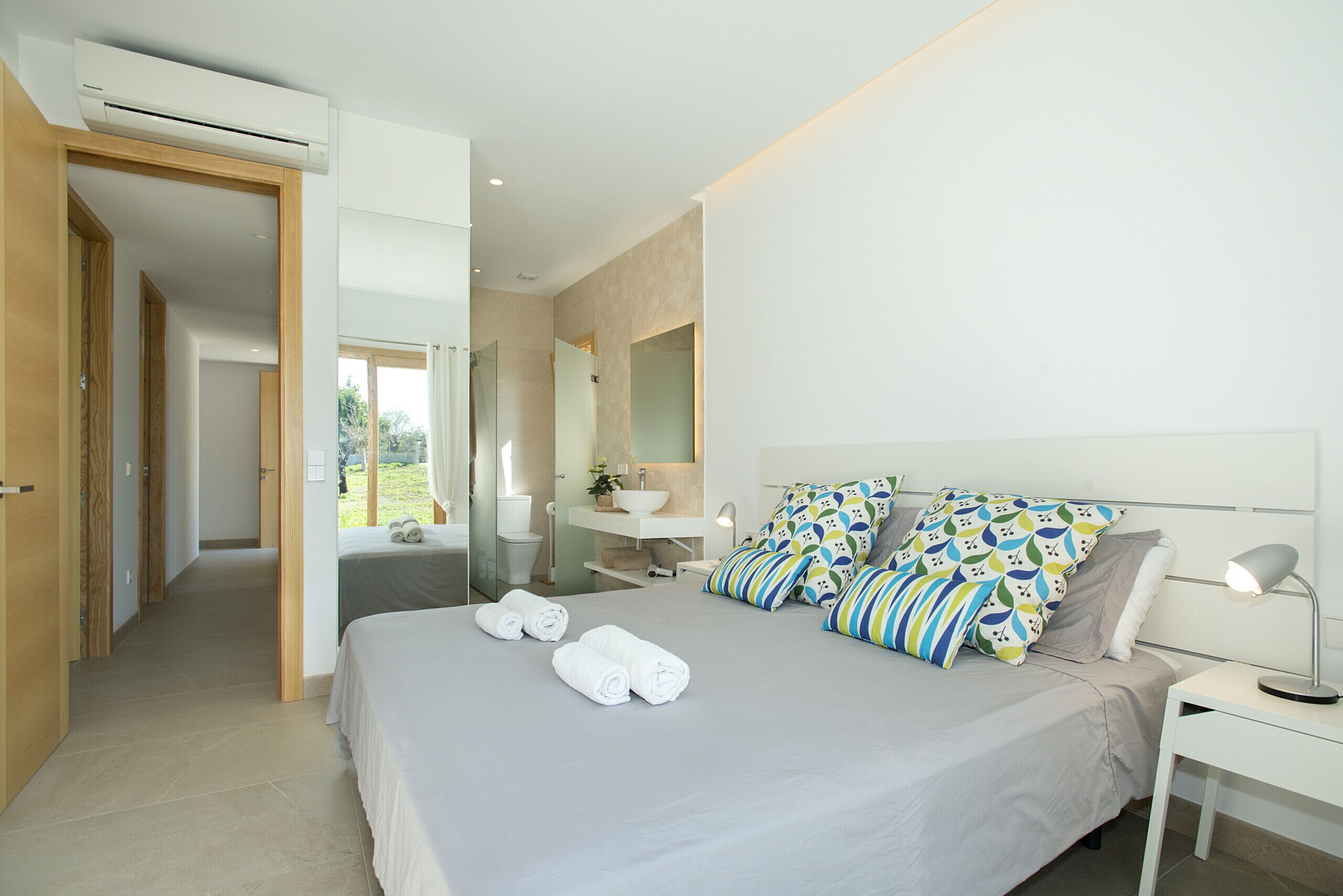 A modern bedroom with a large bed, a bedside table with a lamp, and a bathroom visible through an open door.