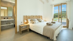 A bedroom with a large bed, wooden headboard, bedside tables, a nightstand, a mirror, and a view of the outdoors. - VILLA MIR - LUXURY RETREAT (Pollensa)