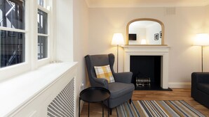 A living room with a fireplace, a chair, a table, and a mirror on the wall. - Victoria Charming Atmosphere (London)