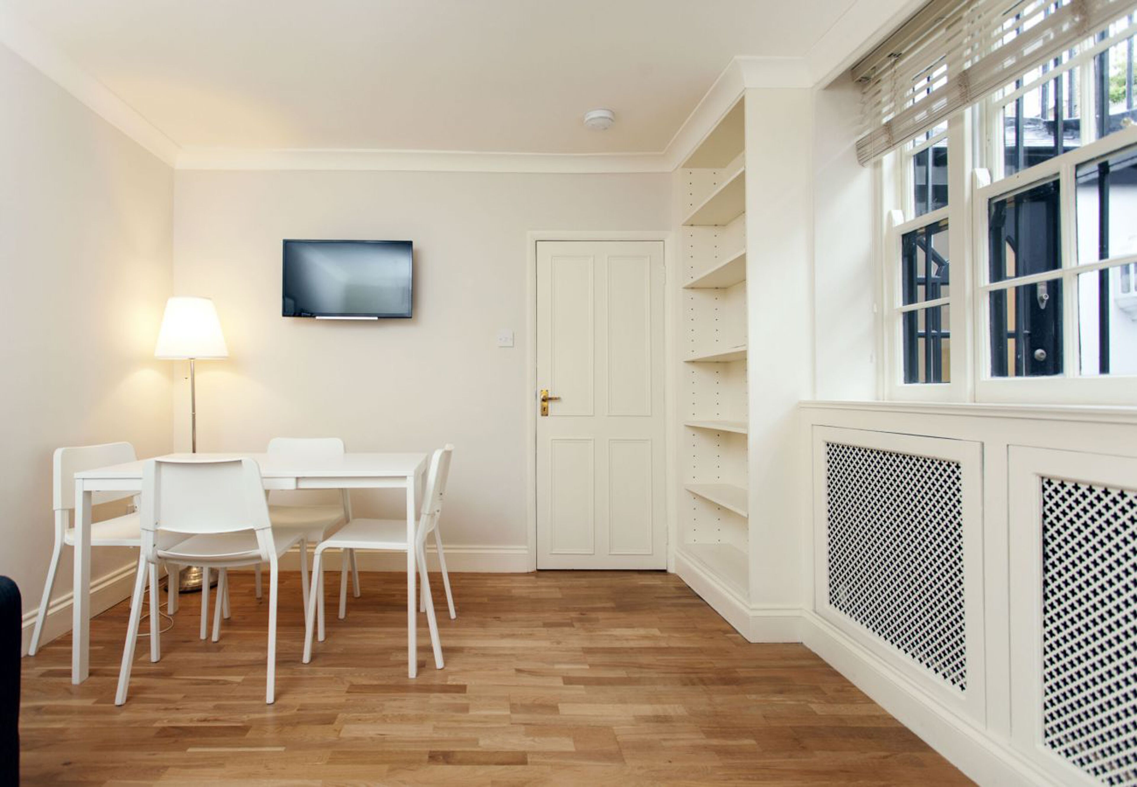 A room with a white table and chairs, a TV mounted on the wall, and a door with a handle.