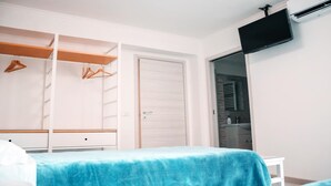 Une chambre à coucher comprenant un lit, une armoire, un téléviseur et une salle de bain visible à travers une porte ouverte.