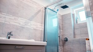 Une salle de bain moderne avec une douche à l’italienne en verre, un lavabo avec un robinet et un sol carrelé.