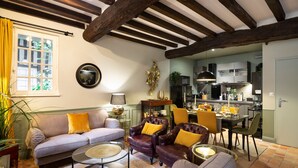 Ein gemütliches Wohnzimmer mit einer Couch, Sesseln und einem Couchtisch. Im Hintergrund ist ein Essbereich mit Tisch und Stühlen zu sehen.