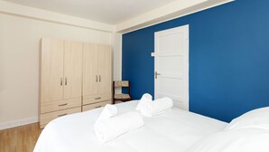 Quarto com cama, duas toalhas enroladas, um guarda-roupa de madeira e parede azul.