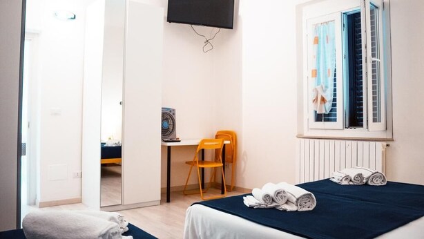 Un dormitorio con cama, escritorio, silla, televisor y ventana con cortinas.