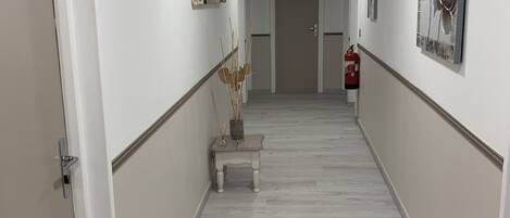Un pasillo moderno y luminoso, con paredes blancas, suelo de madera y obras de arte decorando las paredes.