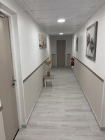 Un pasillo moderno y luminoso, con paredes blancas, suelo de madera y obras de arte decorando las paredes.