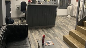 A modern office space with a leather couch, a small table with a magazine, and a reception desk with a computer monitor. - Hotel bon accueil (Oyonnax)