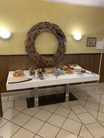 Una mesa de buffet con diversos alimentos y salsas, frente a una pared decorada con una corona de madera y dos luces fijadas a la pared.