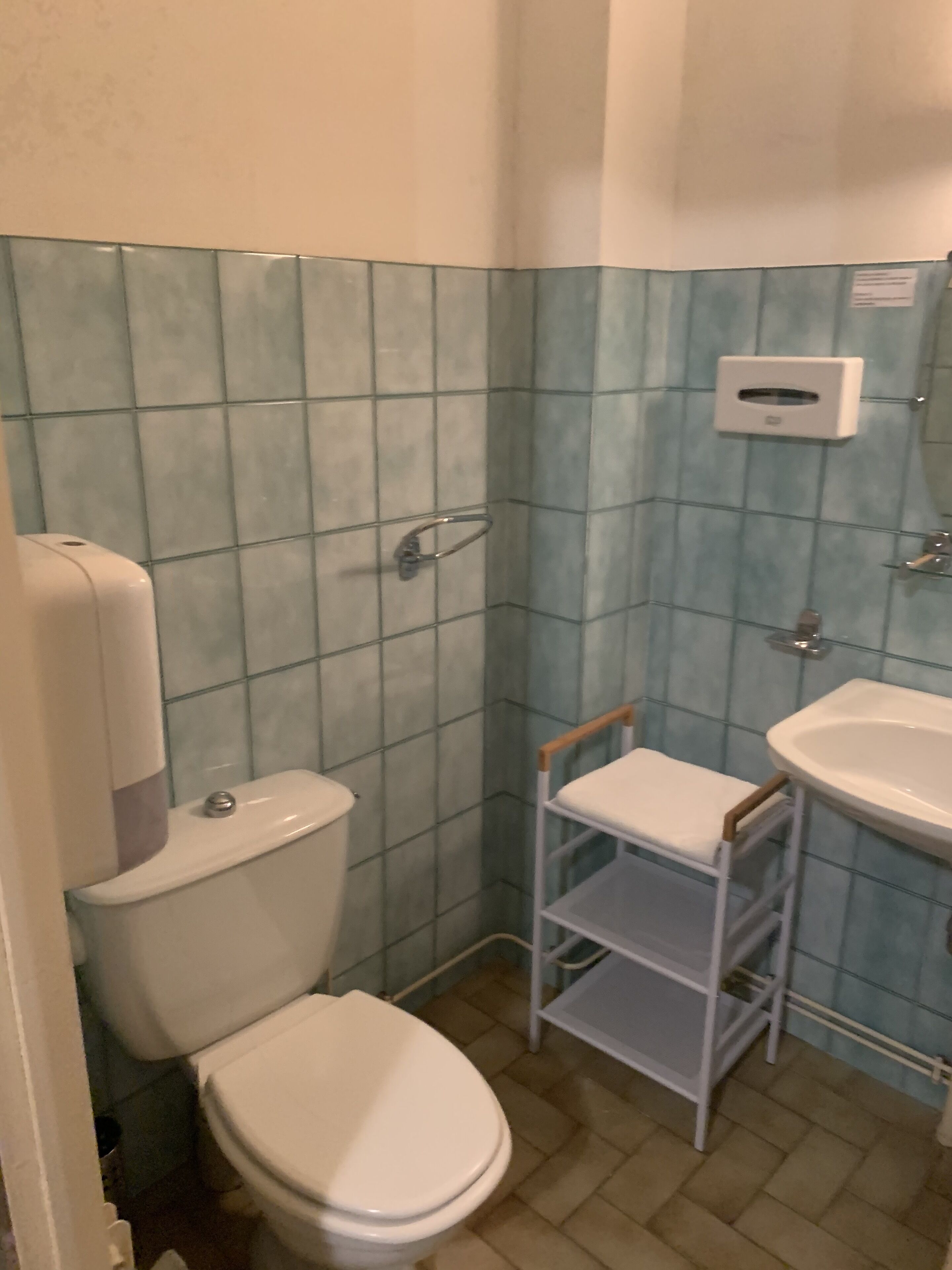 Een badkamer met een toilet, een wastafel en een plank met een stoel.