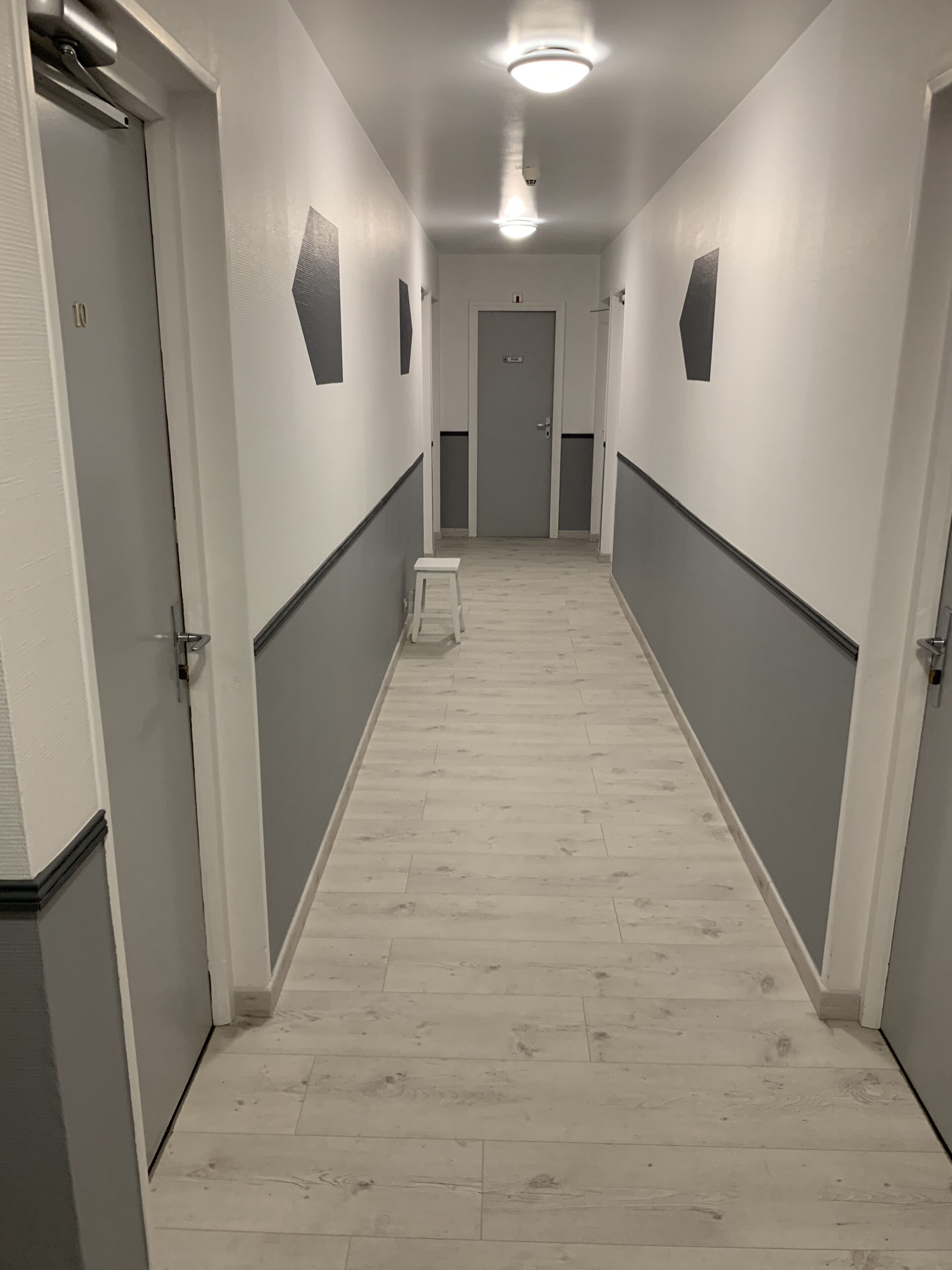 A narrow, well-lit hallway with a wooden floor, white walls, and doors on both sides.